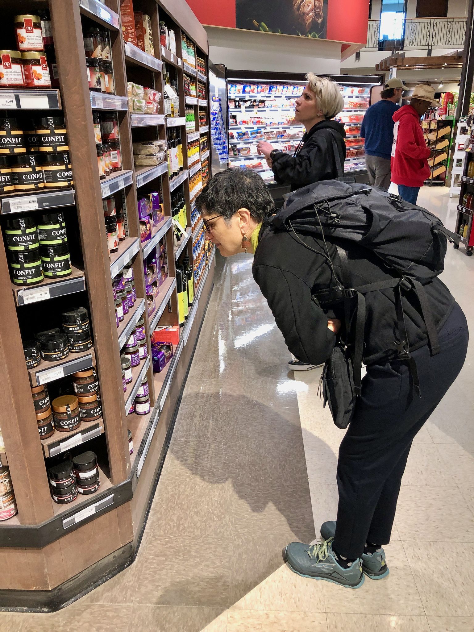 A woman leans in to look at jars of product on a grocery store shelf.