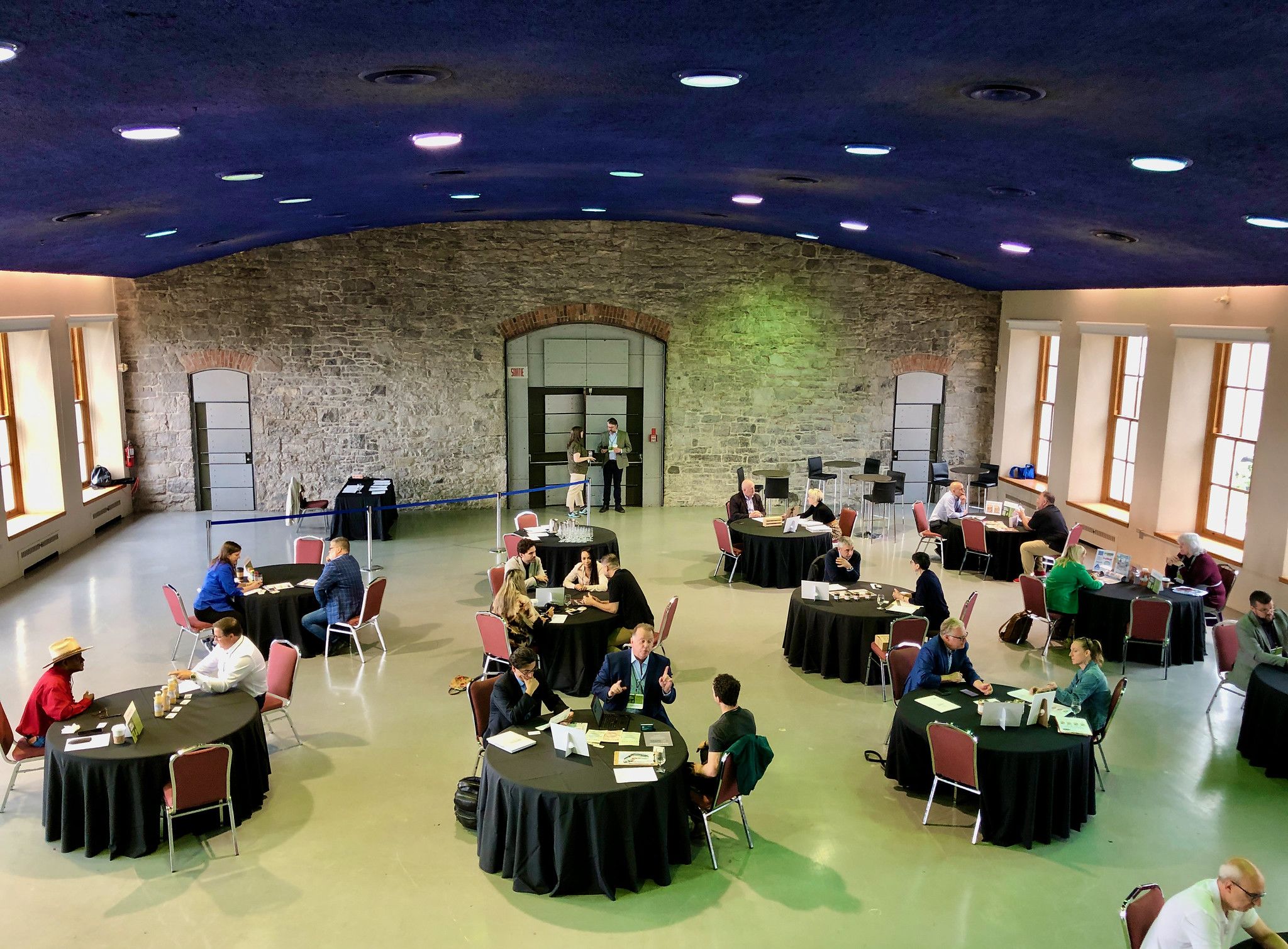 Groups of 2 to 4 people sit around multiple round tables in a large room discussing products.