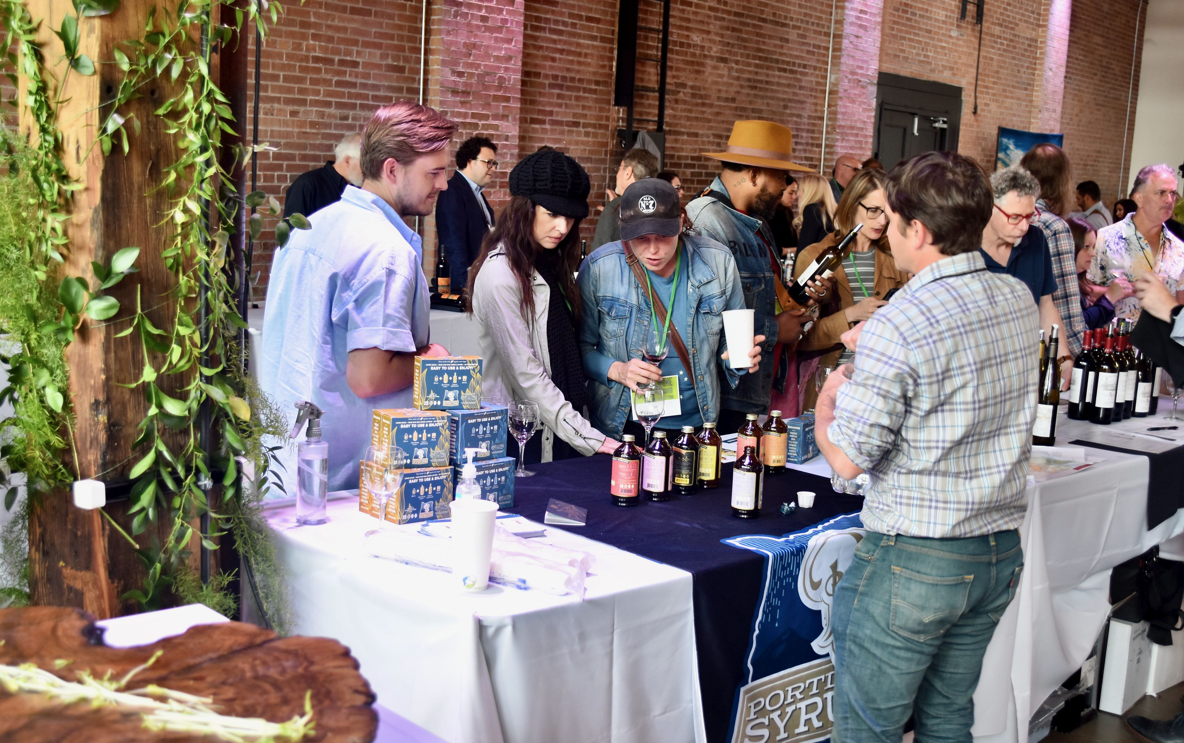 Multiple people stand in front of a table looking at bottles during a trade show.